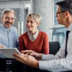 Happy mid adult couple using touchpad with their financial consultant in the office.